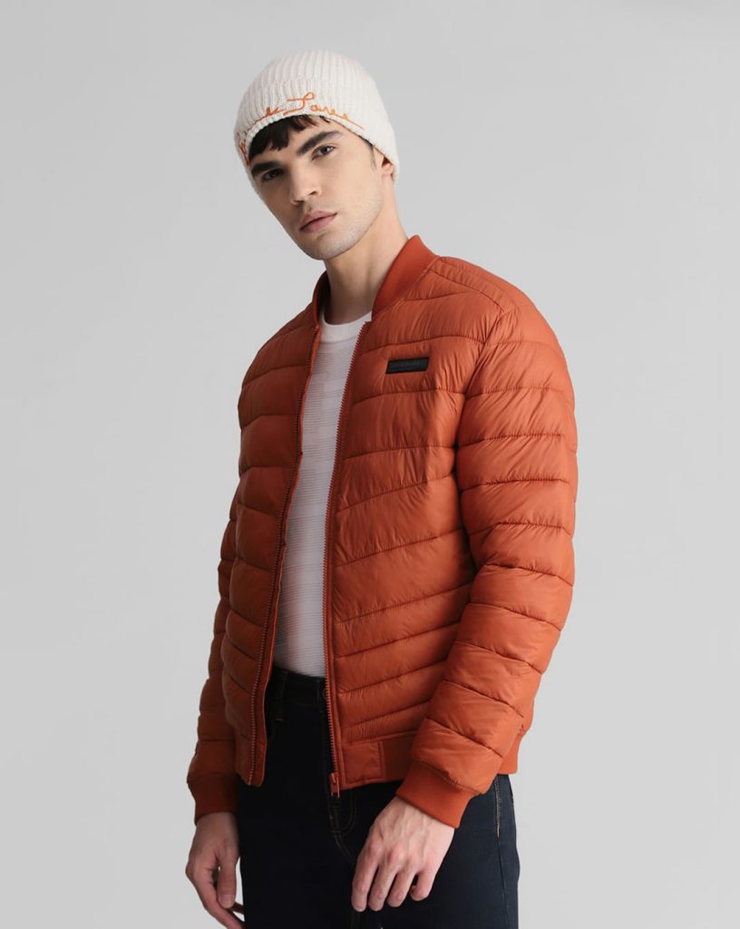 Men's puffer jacket in burnt orange with a white knitted beanie, offering warmth and style for the colder months.